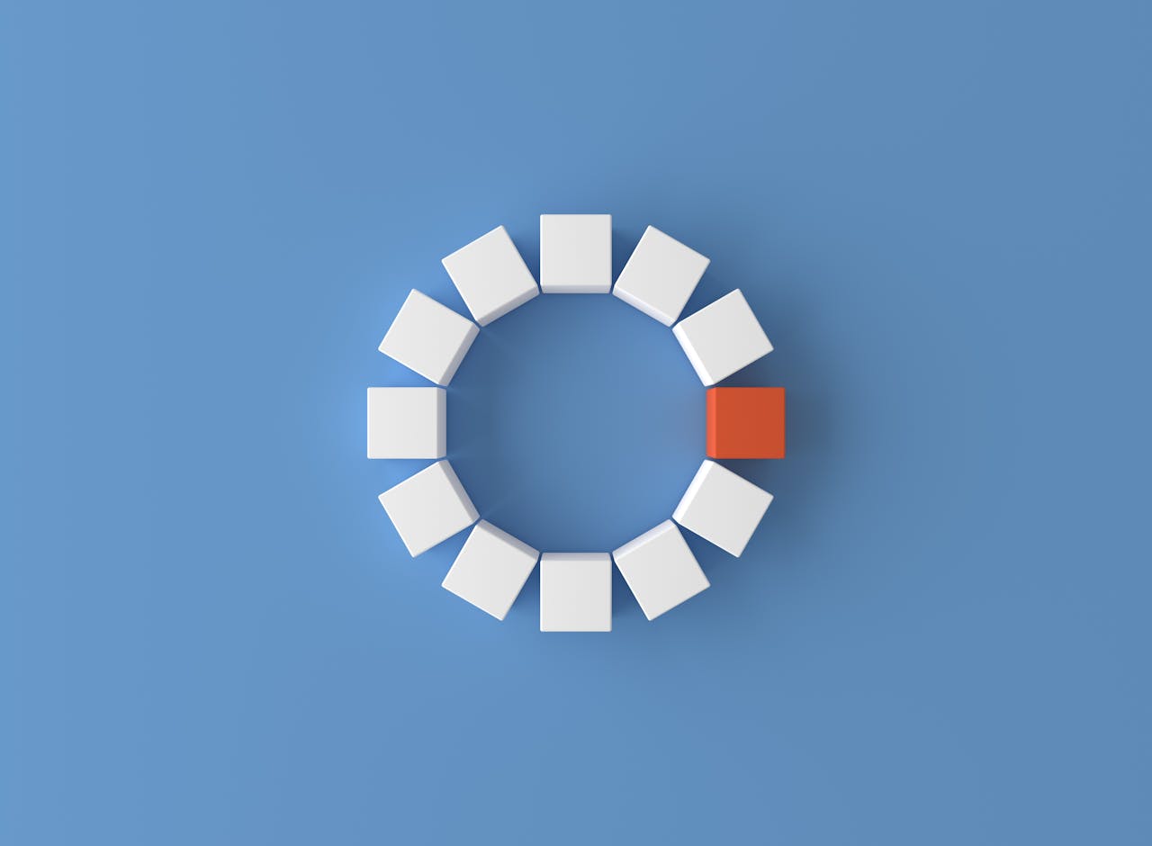 A minimalist 3D render featuring a circle of white cubes with one red cube on a blue background.